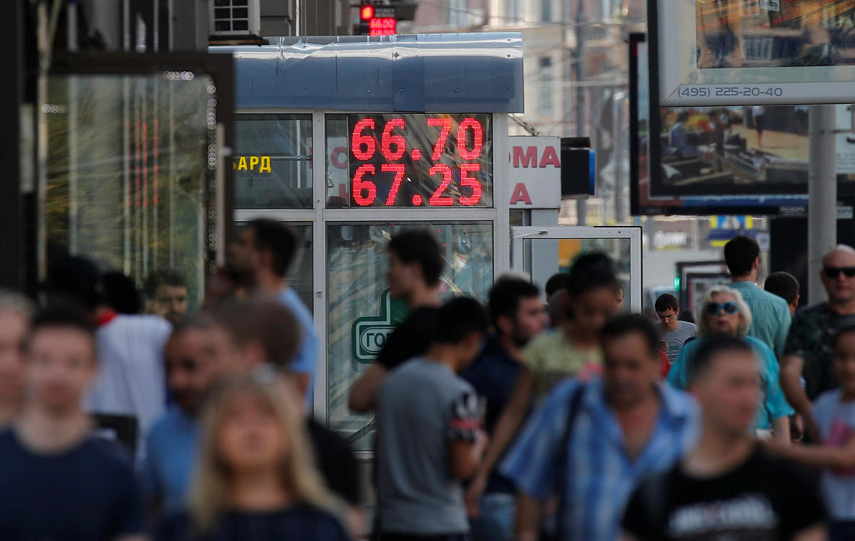 Pedestrians walk by an electronic board showing currency exchange rates of the US dollar against Russian rouble in Moscow on August 10, 2018. Reuters