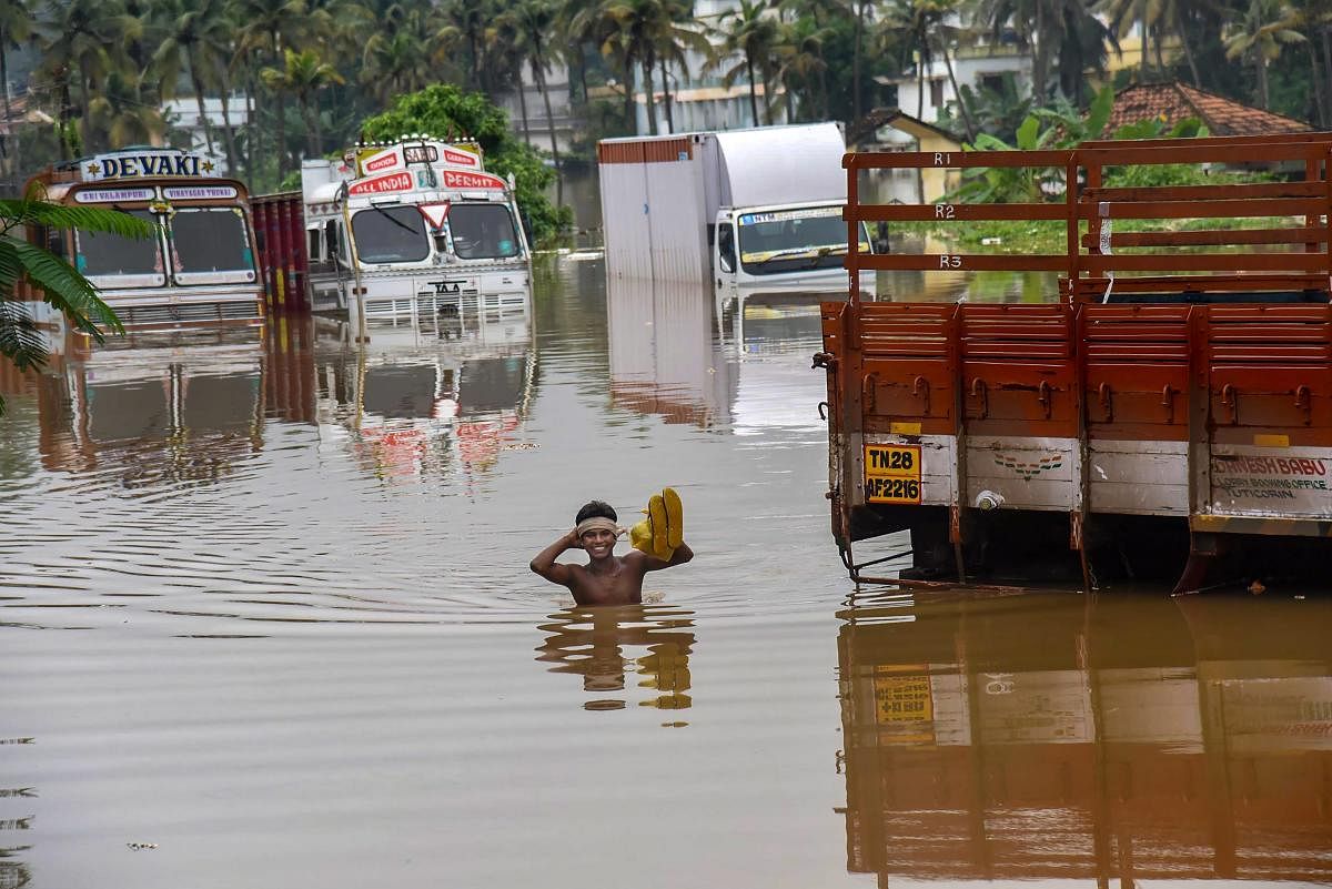 A person stands near submerged trucks on a waterlogged street at a flood-affected region following heavy monsoon rainfall, in Kochi on Thursday. PTI