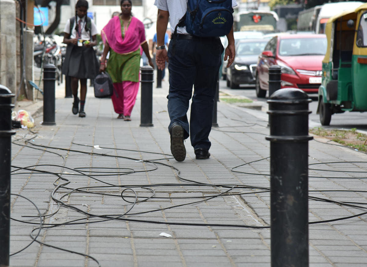 Pedestrians struggling to free walk due to BBMP uncleared of unauthorized optical fibre cables (OFC) after removal drive on Cunningham road in Bengaluru on Tuesday. Photo by B K Janardhan