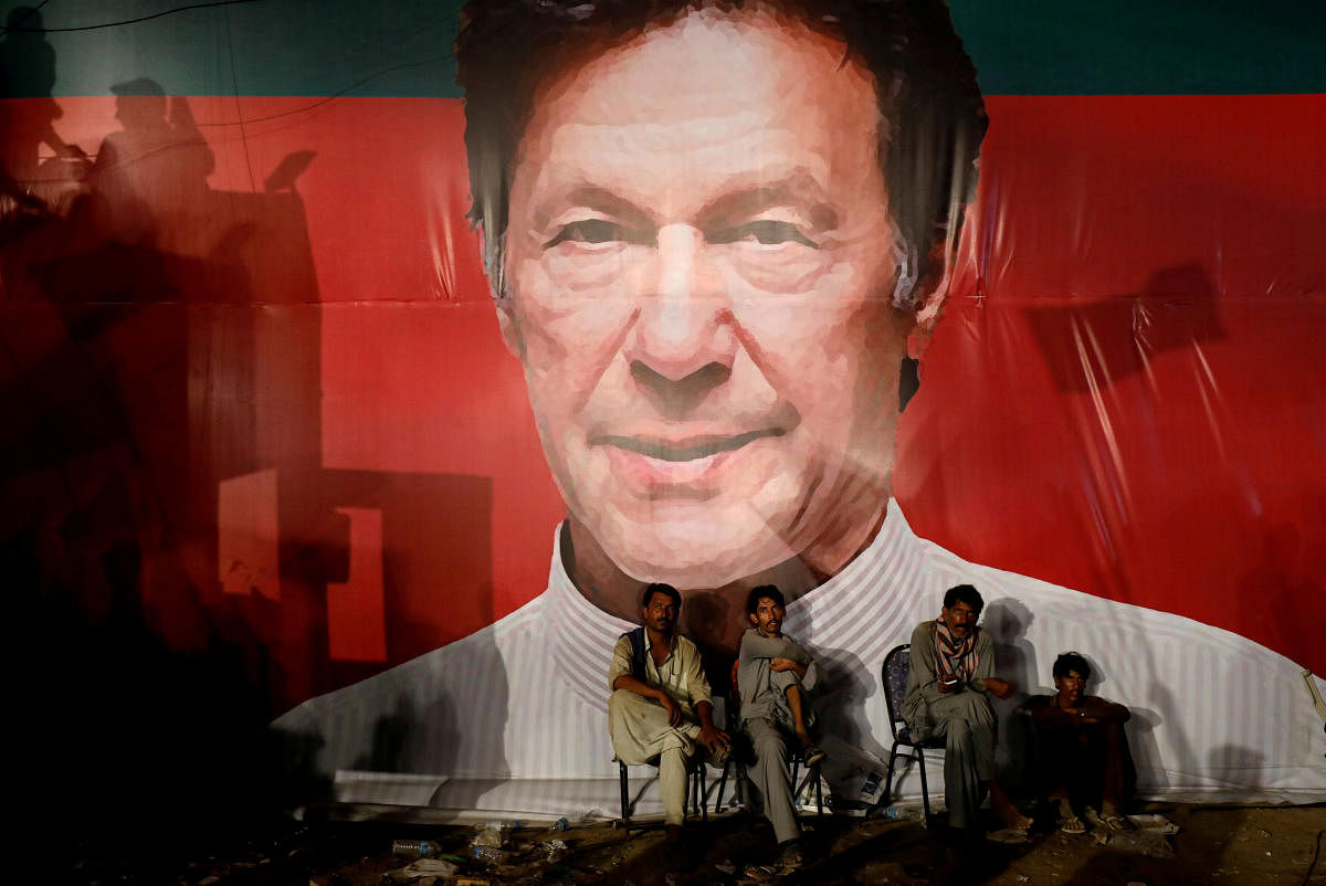 Labourers, sit under a wall with a billboard displaying a photo of Imran Khan, chairman of the Pakistan Tehreek-e-Insaf (PTI), political party, as they listen to him during a campaign rally ahead of general elections in Karachi, Pakistan. (Reuters File Photo)