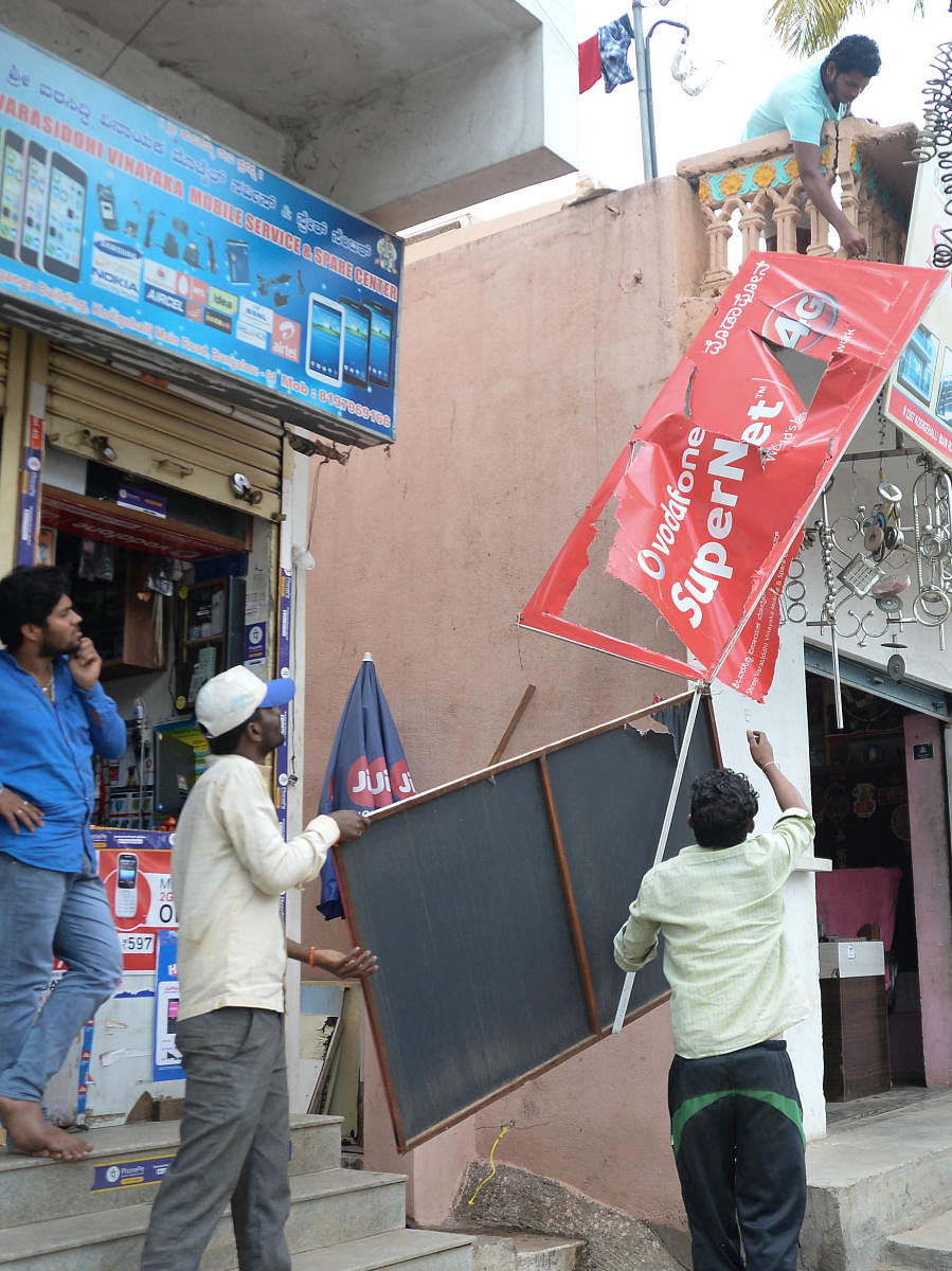 BBMP workers remove flex boards on Kodigehalli Main Road on Monday. DH PHOTO