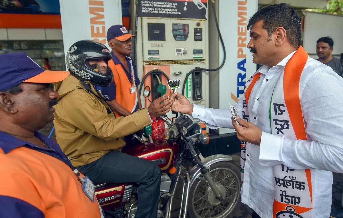 A Nationalist Congress Party (NCP) worker gives away a lotus motif to a motorcyclist at a petrol pump during a protest against the fuel price hike, in Mumbai on Tuesday, August 28, 2018. (PTI Photo/Shashank Parade)