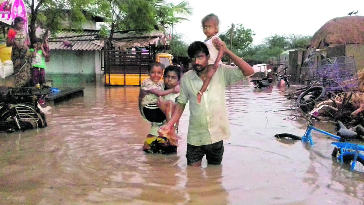 A man carries his children to safety on a waterlogged street at Handihal village in Ballari taluk on Monday. DH Photo