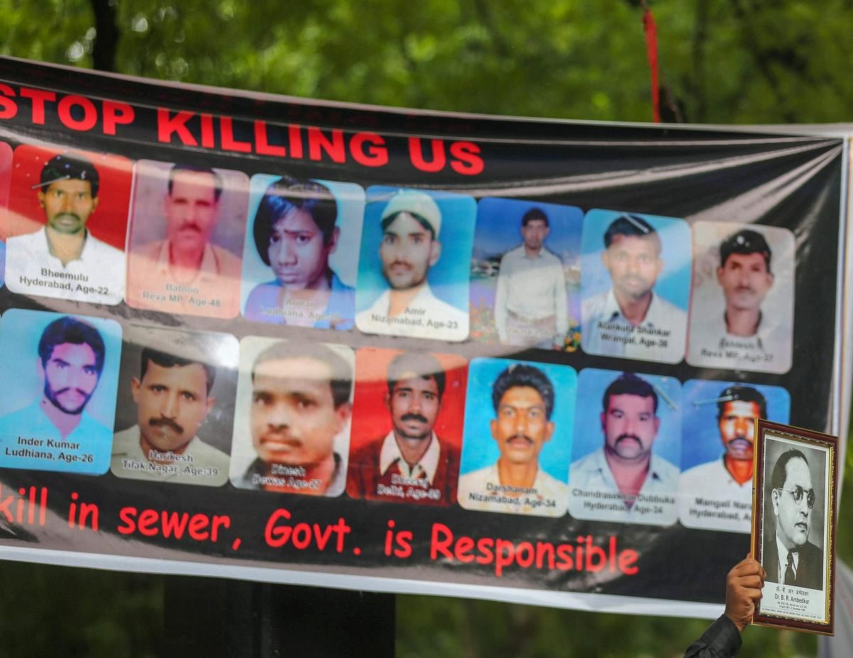 A protestor displays a photo of BR Ambedkar in front-of a banner displaying photos of manual scavengers who lost their lives, during a protest against the violation of Manual Scavenging Prohibition Act 2013, at Jantar Mantar in New Delhi. (PTI Photo)