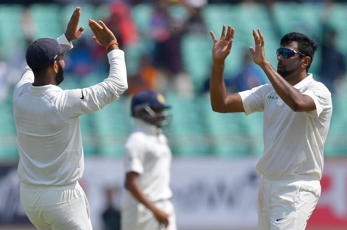 India's Cheteshwar Pujara (L) and Ravichandran Ashwin (R) celebrate after the dismissal of West Indies batsman Keith Brathwaite during the third day's play of the first Test cricket match between India and West Indies at the Saurashtra Cricket Association