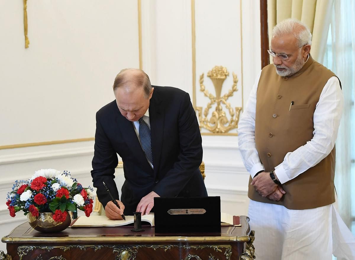 Russian President Vladimir Putin (L) signing the visitors book as Prime Minister Narendra Modi looks on at the Hyderabad House in New Delhi. (Photo by Handout/PIB/AFP)