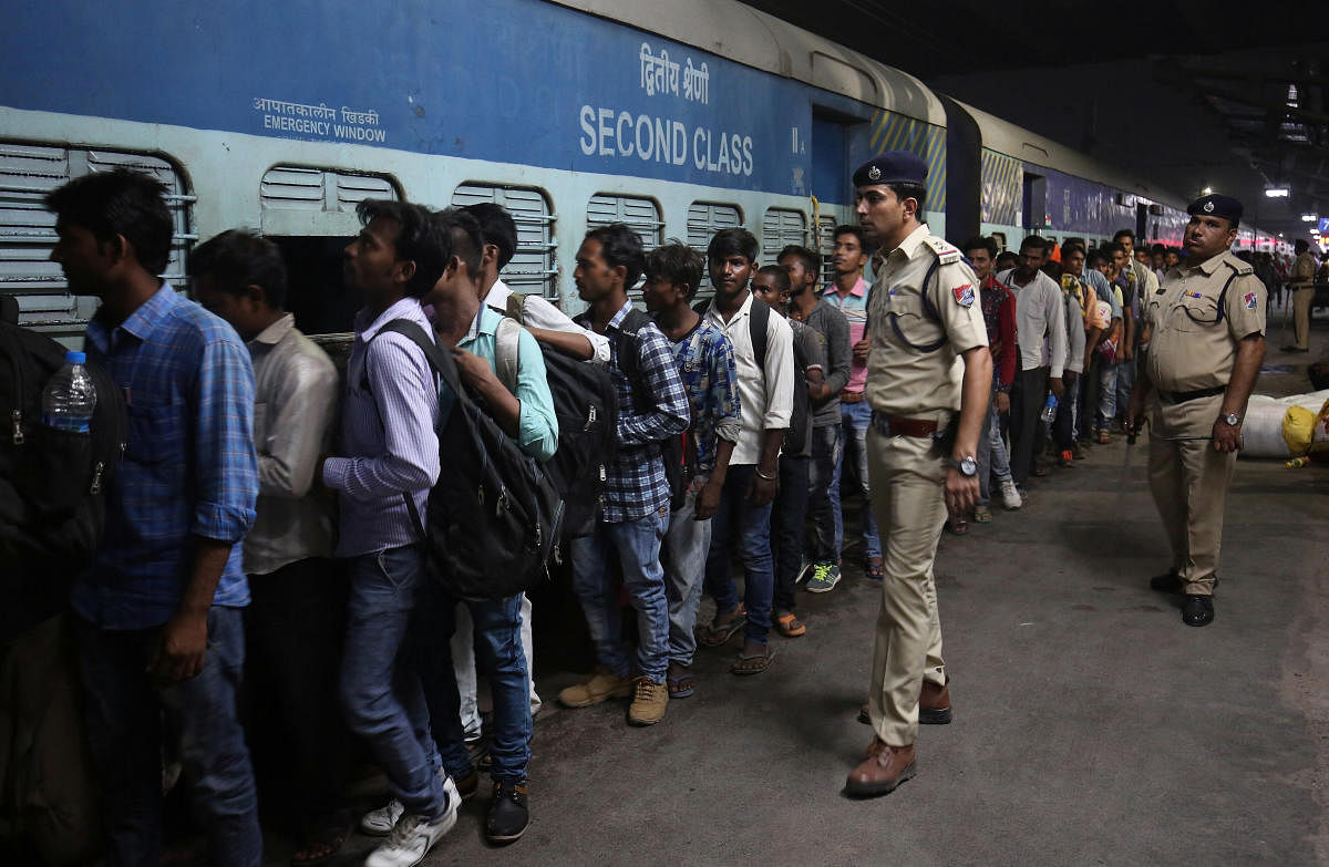 Railway police officers stand guard, as migrant workers from the northern state of Uttar Pradesh board a passenger train to depart from a railway station in Ahmedabad. PTI photo