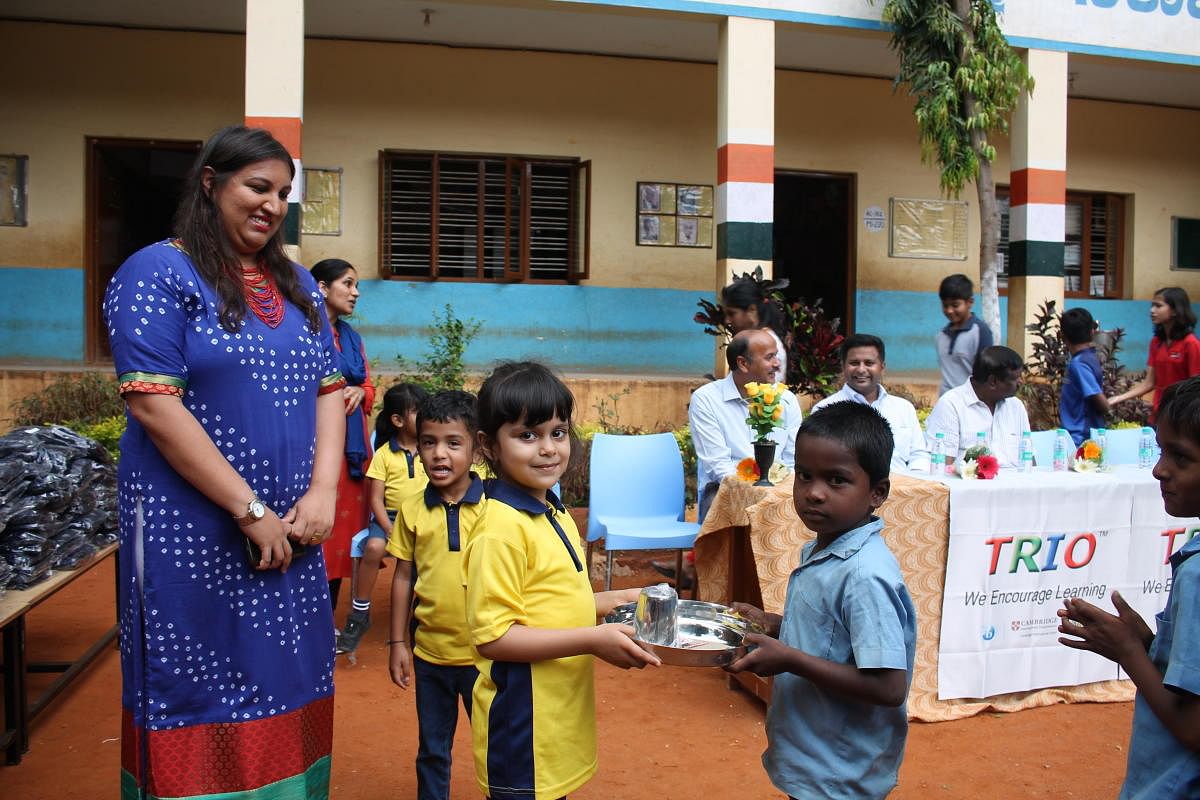 A student of Trio World School gives away a stainless steel plate and glass to a student of Government Primary and Upper Middle School in Kodigehalli as part of the Joy of Giving week recently.