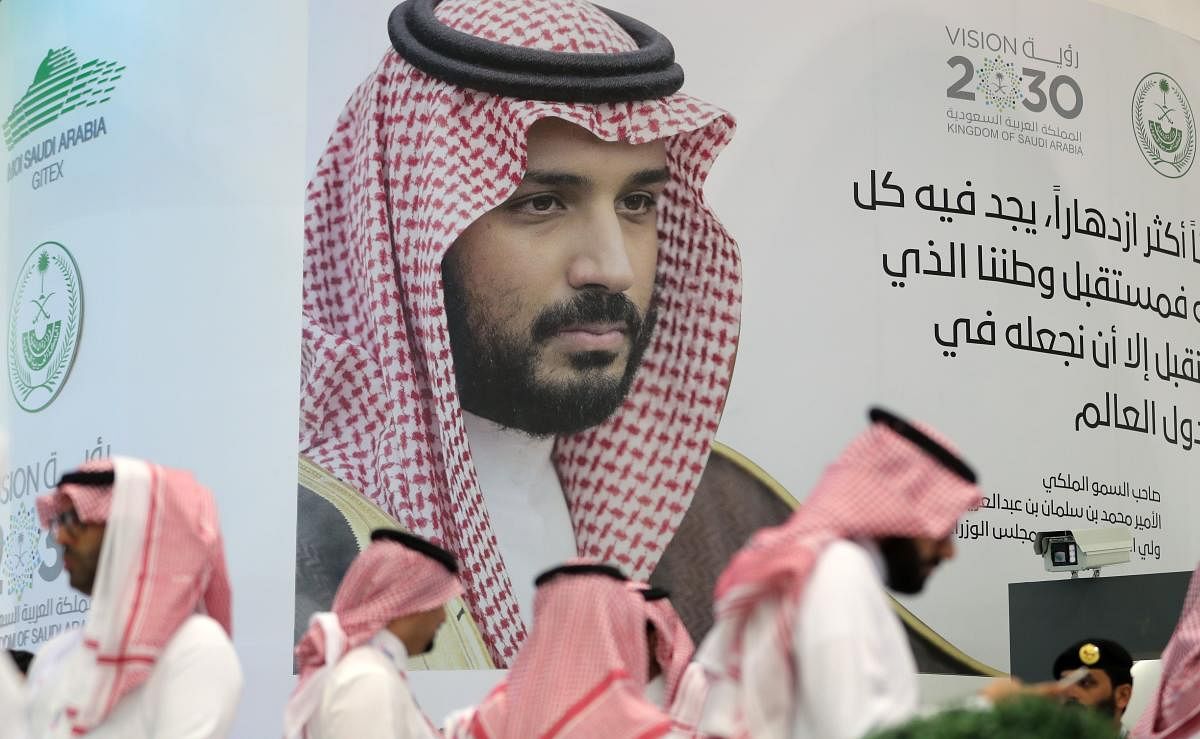 Saudi stand next to a portrait of Saudi Crown Prince Mohammed bin Salman at the Gitex 2018 exhibition at the Dubai World Trade Center in Dubai on October 16, 2018. - Gitex ("Gulf Information Technology Exhibition") is a consumer computer and electronics t