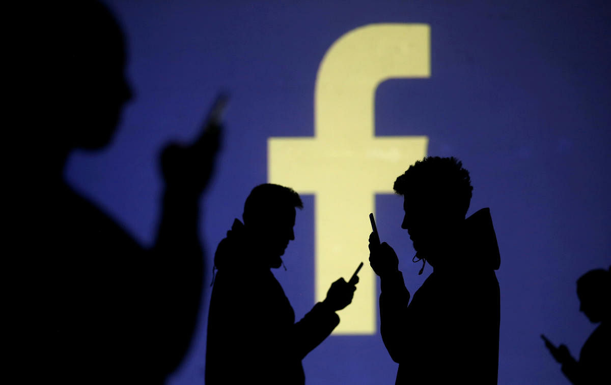 Silhouettes of mobile users are seen next to a screen projection of Facebook logo in this picture illustration. Reuters