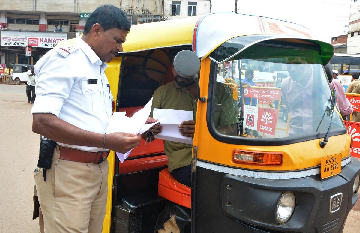 A traffic police check documents of an autorickshaw at Chennamma Circle area in Hubballi on Friday, during the autorickshaw checking drive.