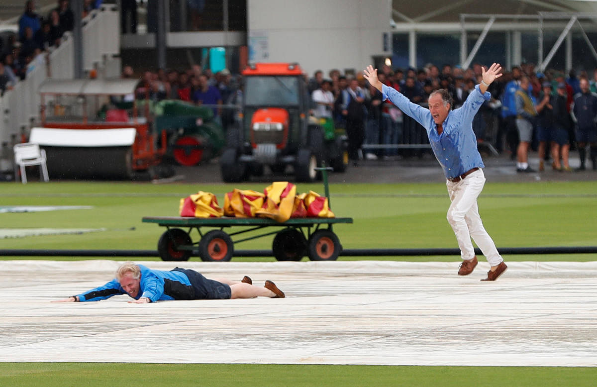 Spectators run onto the pitch and slide on the covers during rain delay on the opening day of the second Test at Lord's. Reuters