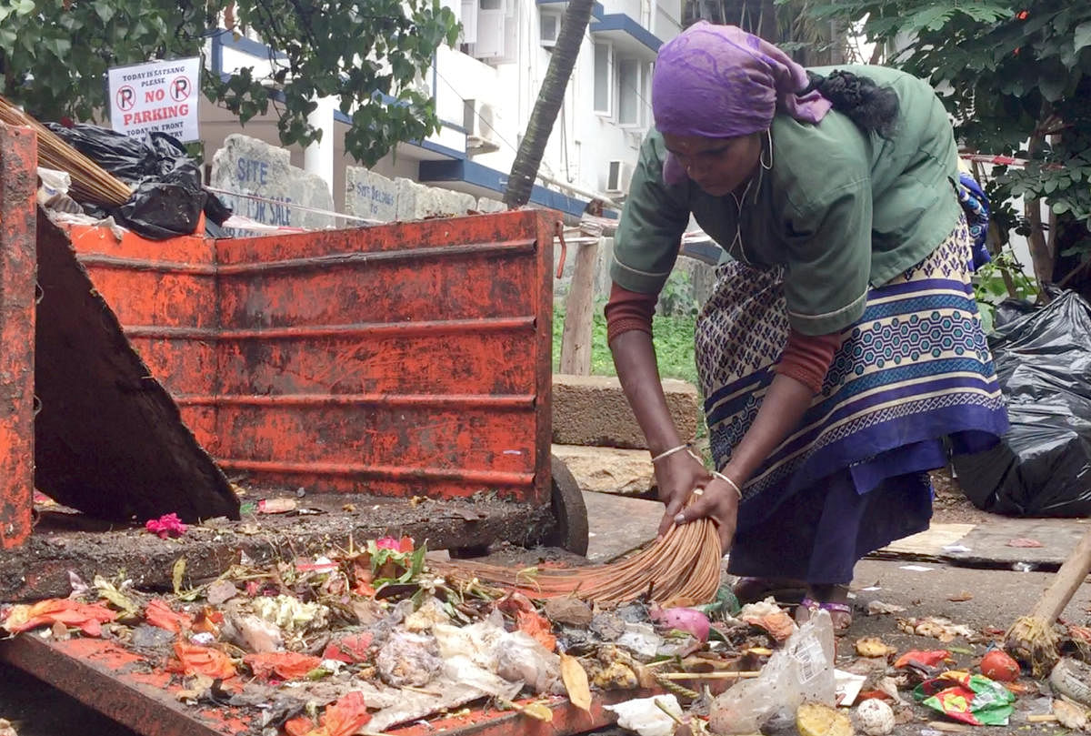 A pourakarmika collects waste at Indiranagar on Wednesday. DH Photo/Grace Hauck