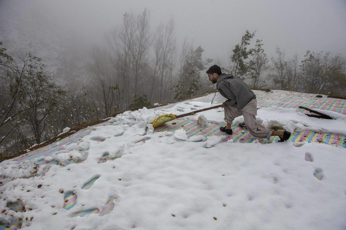 A man clears snow from the roof top of his mud-house on the out skirts of Srinagar. PTI
