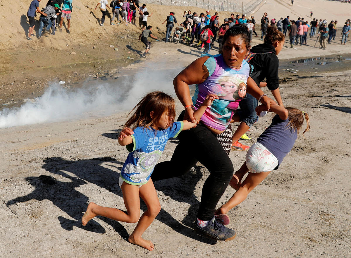 A migrant family from Honduras, part of a caravan of thousands travelling from Central America en route to the United States, runs from tear gas released by US border patrol near the fence between Mexico and the United States in Tijuana, Mexico, on Novemb