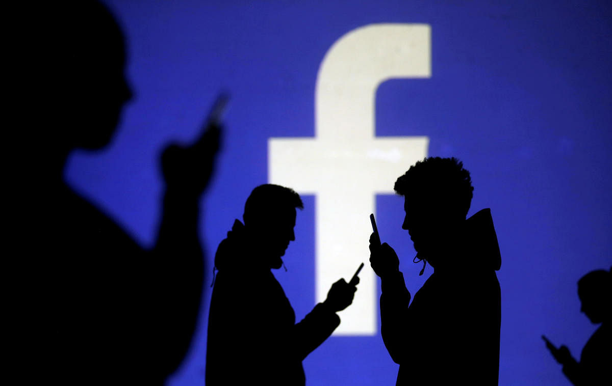 Silhouettes of mobile users are seen next to a screen projection of the Facebook logo in this picture illustration. Reuters file photo