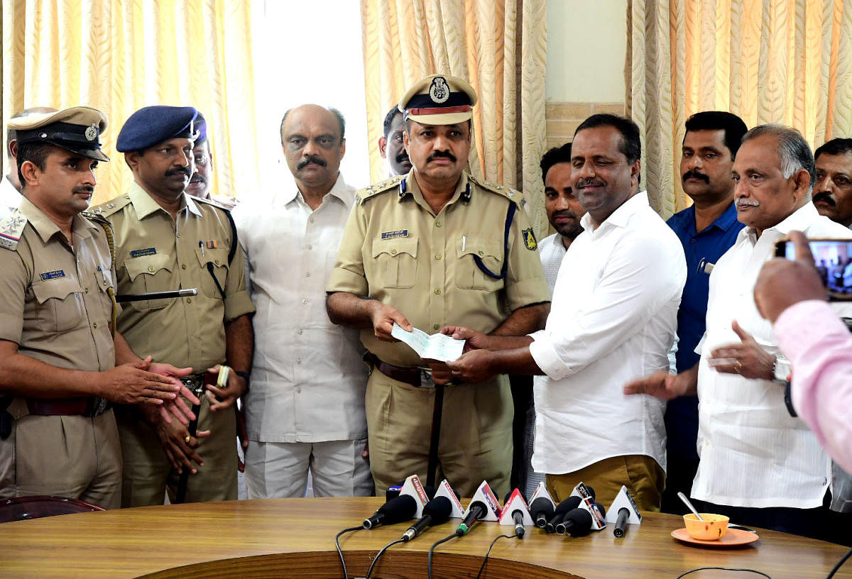 District In-charge Minister U T Khader hands over a cheque for Rs 1 lakh as a reward for Panambur police, to City Police Commissioner T R Suresh, in Mangaluru on Friday. 