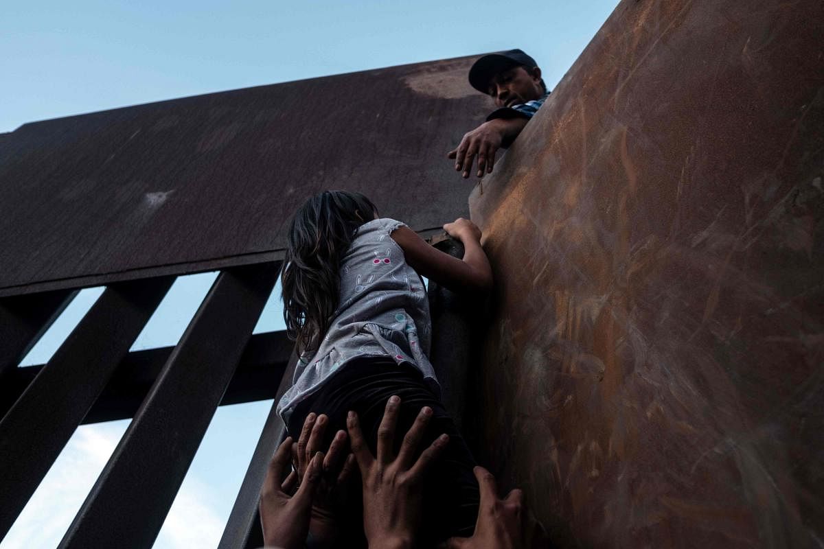 A girl who has been travelling in a caravan of Central American migrants hoping to get to the United States, is helped to climb the metal barrier separating Mexico and the US to cross from Playas de Tijuana in Mexico into the US. AFP
