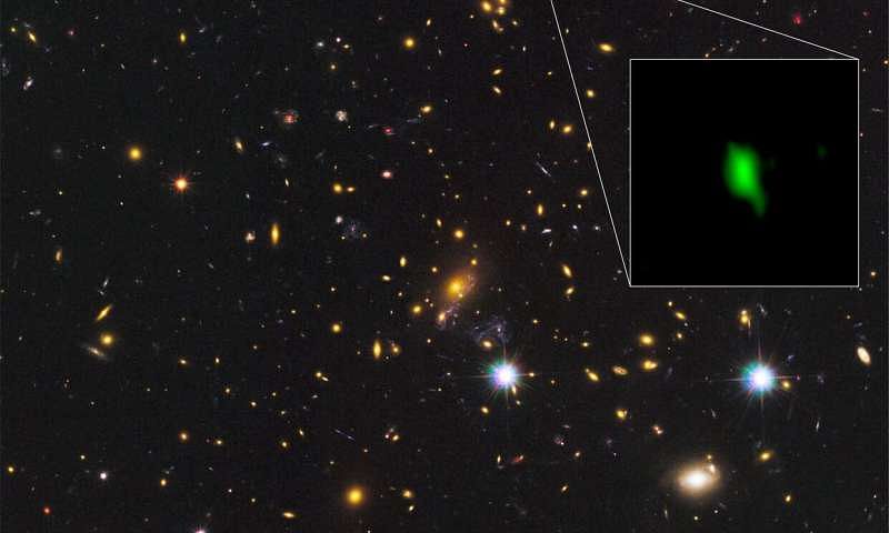 The galaxy cluster MACS J1149.5+2223 taken with the NASA/ESA Hubble Space Telescope and the inset image is the galaxy MACS1149-JD1 located 13.28 billion light-years away observed with ALMA. Here, the oxygen distribution detected with ALMA is depicted in green. Credit: ALMA (ESO/NAOJ/NRAO), NASA/ESA Hubble Space Telescope, W. Zheng (JHU), M. Postman (STScI), the CLASH Team, Hashimoto et al.  