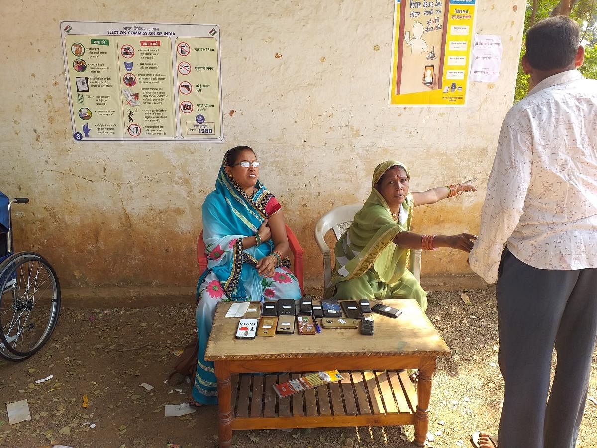Two women guarding the mobile phones of electors who have gone into the booth to vote, at 47-Dharsiwa in Barounda on the outer limits of Raipur. DH PHOTO