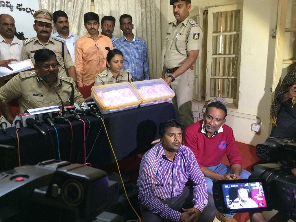 Police Commissioner D C Rajappa giving information about fake currency seized in Belagavi on Tuesday. Accused are seen sitting.