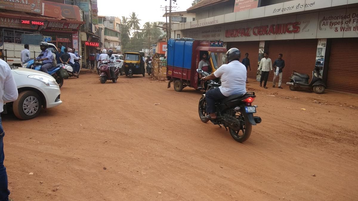 Vehicle users and pedestrians struggle to pass through Nellikayi Road-Mission Street Junction in Mangaluru, where the road is not yet asphalted.