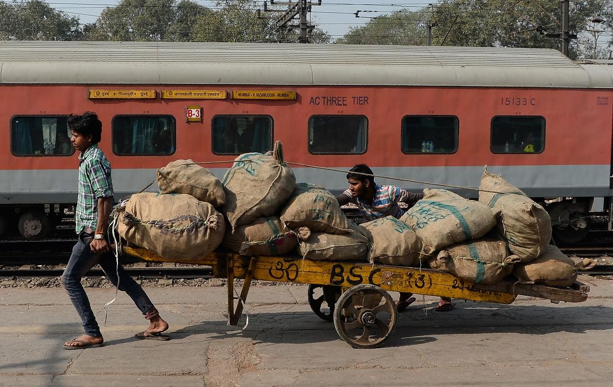 TOPSHOT - Indian labourers transport goods loaded on a handcart at a railway station in New Delhi on February 1, 2018. / AFP PHOTO / SAJJAD HUSSAIN