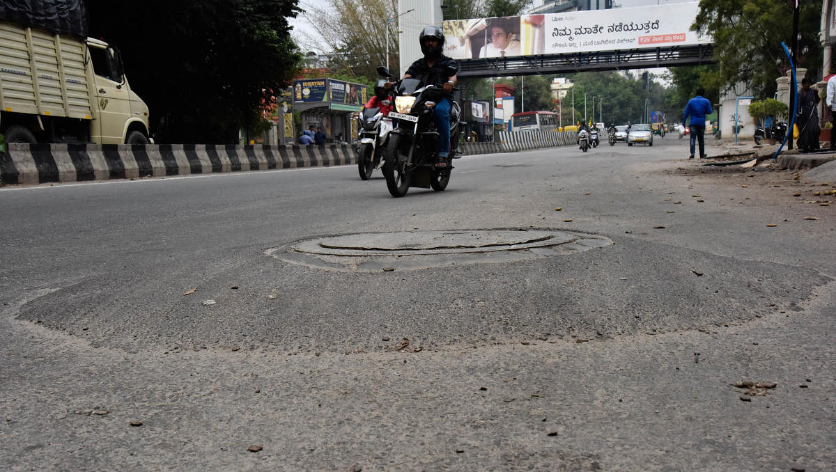 Manholes in many places are raised many inches above the road level. This one is on Kasturba Road in the heart of the city. The condition on roads in the interior neighbourhoods is worse. DH Photos by Janardhan B K and s k dinesh
