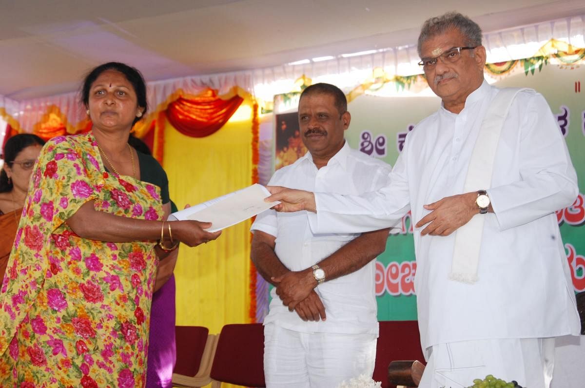 Dharmasthala Dharmadhikari D Veerendra Heggade hands over a cheque to a victim of natural calamity, as a part of the assistance programme under SKDRDP, in Madikeri on Thursday.