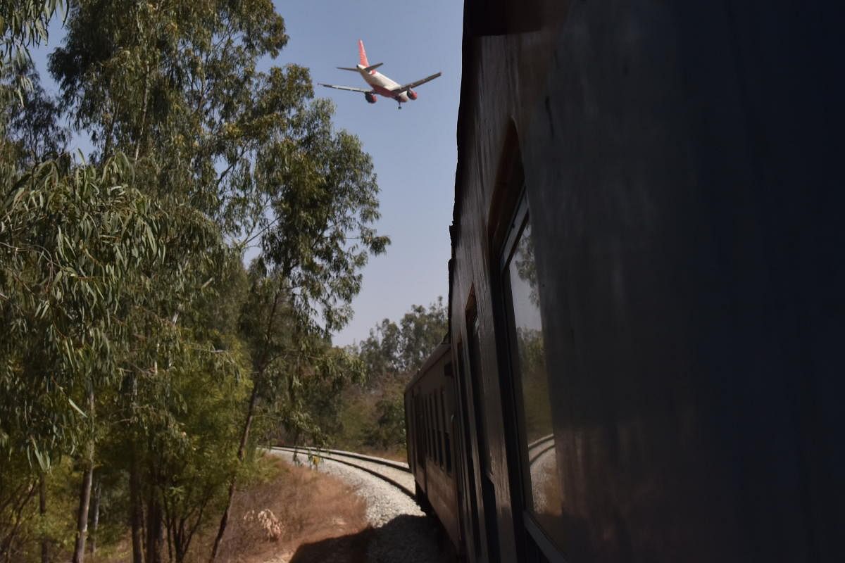 A flight about to land at the Kempegowda International Airport, as a DEMU train passes through an existing track close to the airport perimeter wall.