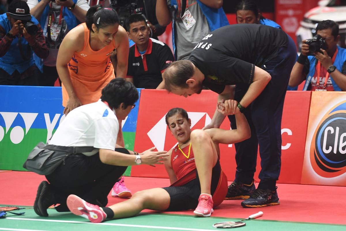 Carolina Marin of Spain (C) reacts to an injury that forced her to retire while playing against Saina Nehwal of India (top L) in their women's singles final match at the 2019 Daihatsu Indonesia Masters tournament in Jakarta on January 27, 2019. (AFP)