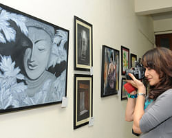 A Young girl clicks a picture of paintings displayed at the Karnataka Chitra kala Parishath (CKP). DH photo