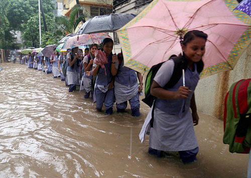 Children wade through a waterlogged road after heavy rain in Thane on Saturday. PTI