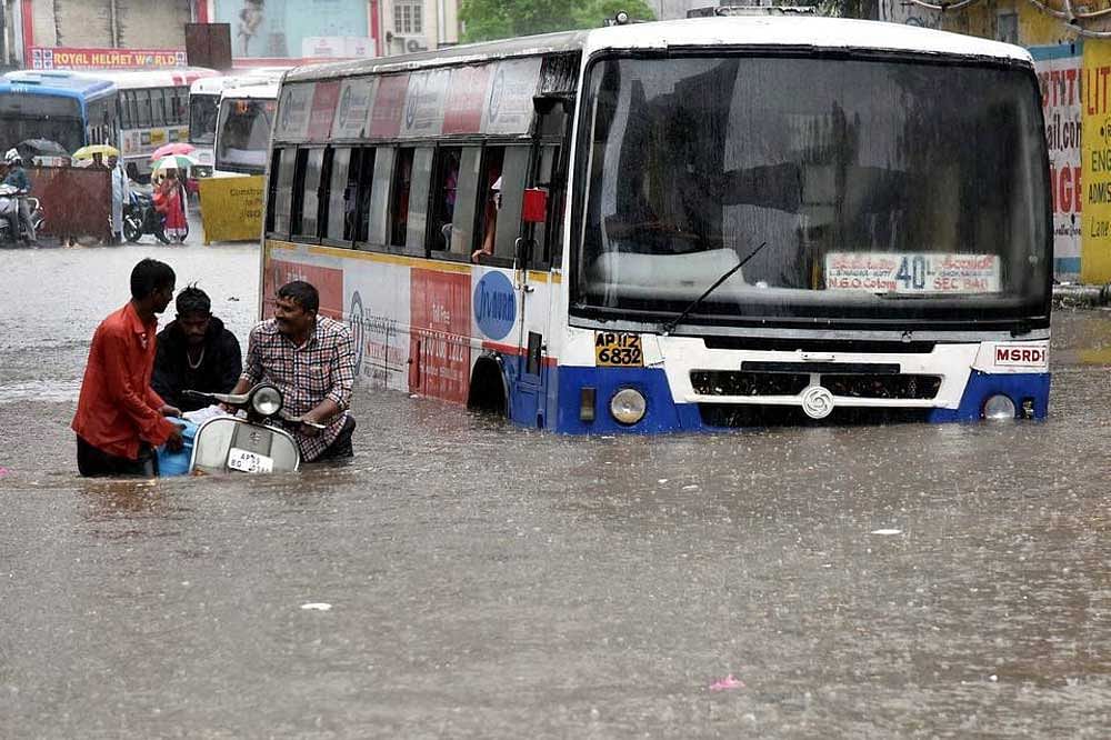 A bus lies half-sunk as two men try to drag a scooter amidst floods caused by heavy rains. DH photo.
