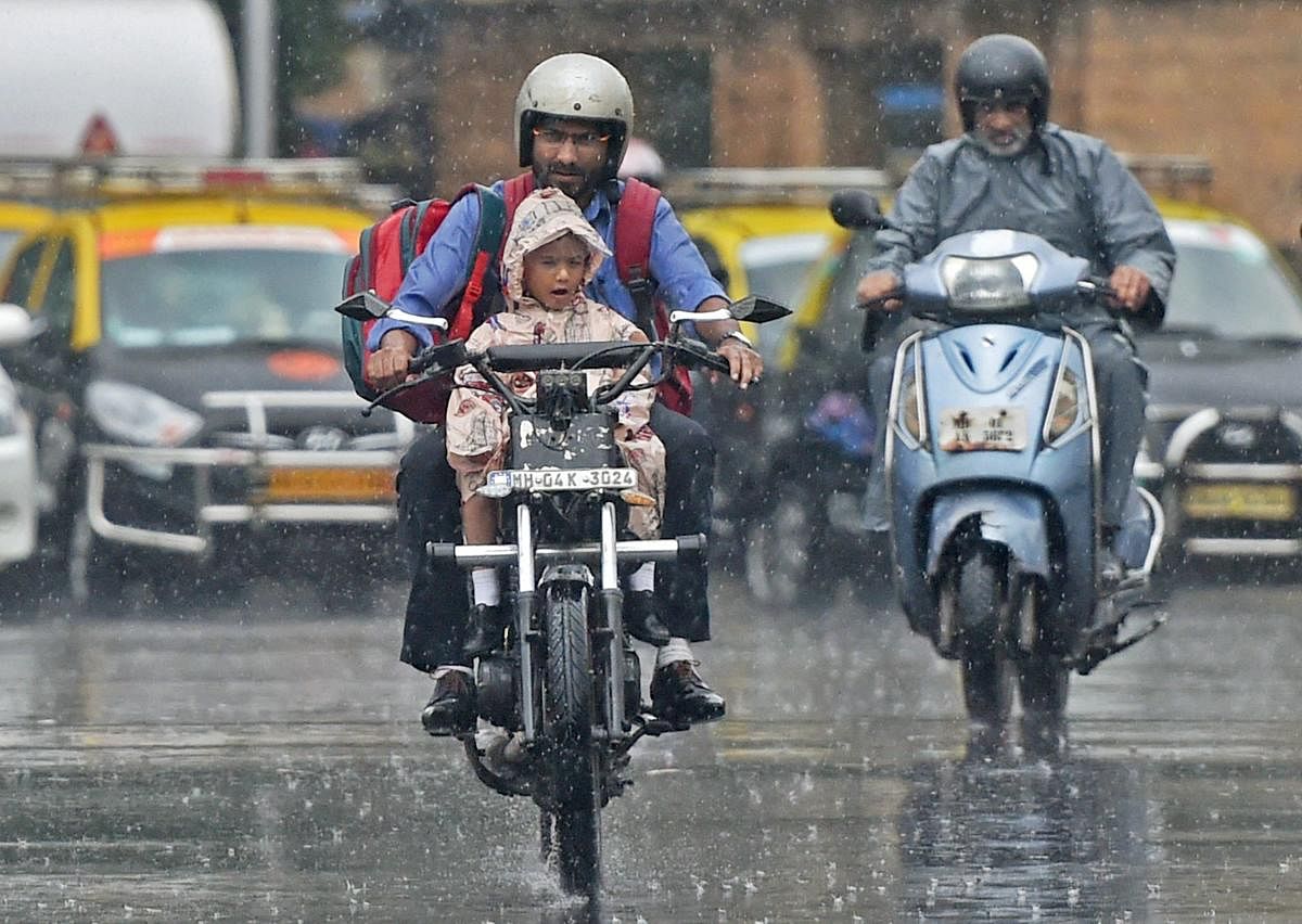A man carries his child home from school on a motorcycle amid a downpour in Mumbai on Tuesday. PTI