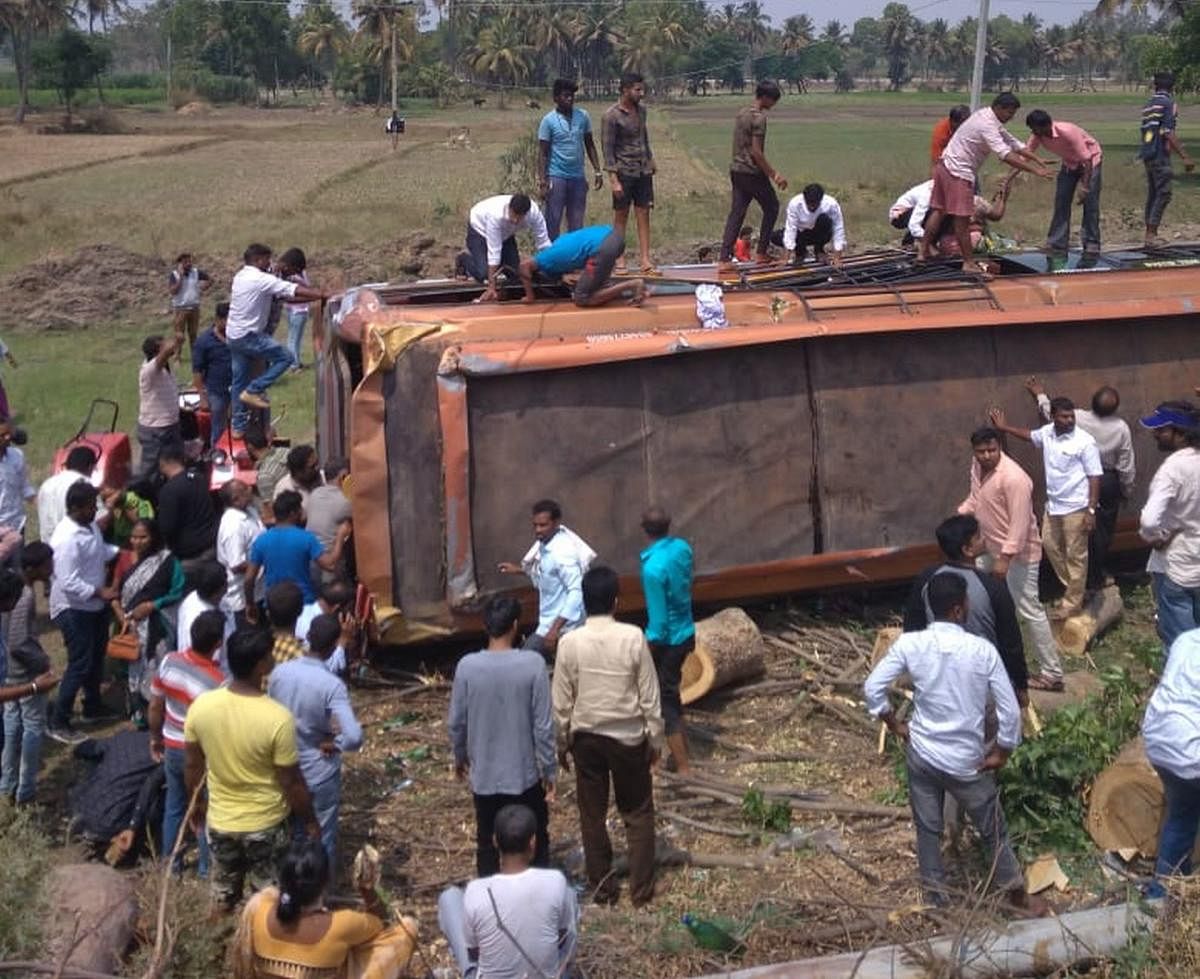 Locals rescue the passengers from the bus that turned turtle in Maddur, Mandya district, on Sunday. DH PHOTO