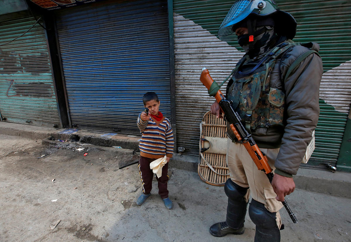A boy plays with his toy pistol next to an Indian policeman standing guard in front of closed shops during a strike called by Kashmiri separatists against the arrest of Yasin Malik in Srinagar. Reuters photo