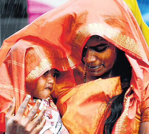 safe in her arms: A woman with her child is caught in the rain at Kalasipalya bus stand  on Wednesday. dh photo/s k dinesh