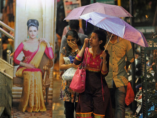 People walk through the rain under the shelter of their umbrellas at Jayanagar 4th block Bus Stand in Bengaluru on Saturday. DH photo