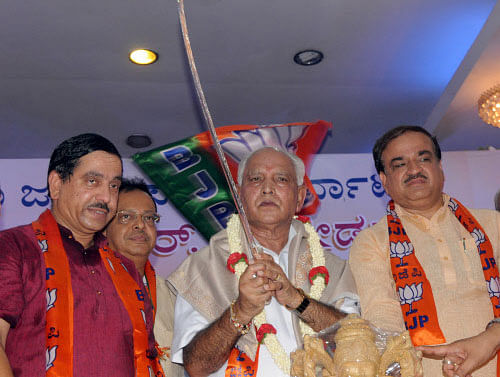 Former Chief Minister Yeddyurappa is presented a silver sword by BJP leaders during the public rally organised to mark his coronation as the new state BJP president in Bengaluru on Thursday. Outgoing president Pralhad Joshi and Union Minister Ananth Kumar are also seen. DH PHOTO