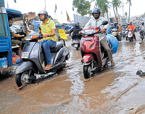 Motorists struggle to drive on a heavily damaged road in City Market, which has not been  repaired for many days, causing heavy traffic jams, on Tuesday. DH Photos