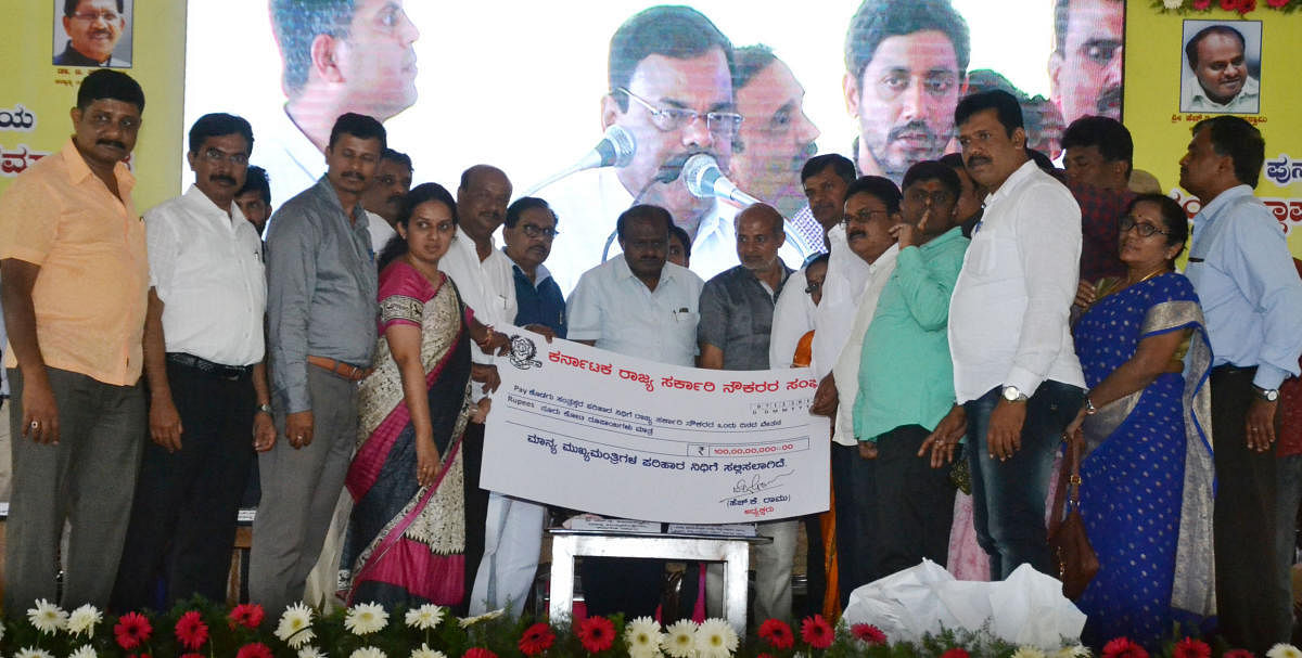 Members of State Government Employees’ Association hand over a cheque for Rs 100 crore to Chief Minister H D Kumaraswamy towards Chief Minister’s Relief Fund at Jambur in Somwarpet taluk on Friday.