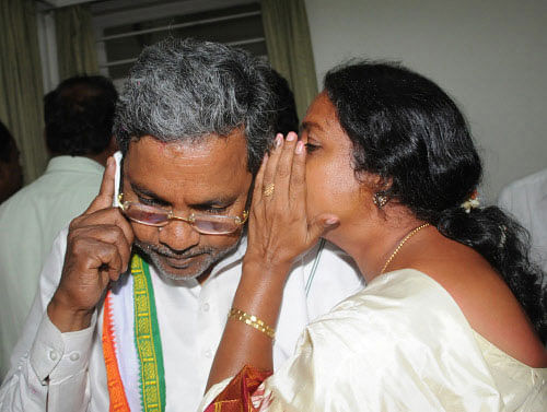 Newly elected MLA Umashree whisper into CM designated Siddaramaiah's ear at his official house in Bangalore on Friday. DH photo