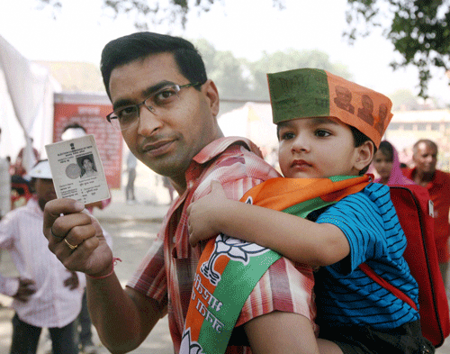 A BJP supporter with his son displays his voter identity card before casting his vote at a polling station in Lucknow on Wednesday. PTI Photo