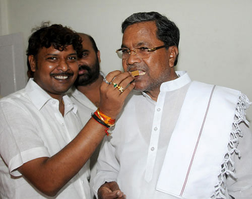 A file picture of Rakesh, son of Chief Minister Siddaramaiah, offering him a sweet after the announcement of Siddaramaiah's name for the chief minister's post in Bengaluru in May 2013. DH PHOTO