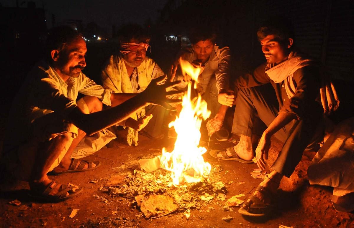 People beat the biting cold at a roadside fireplace near the central bus stand in Vijayapura. DH PHOTO