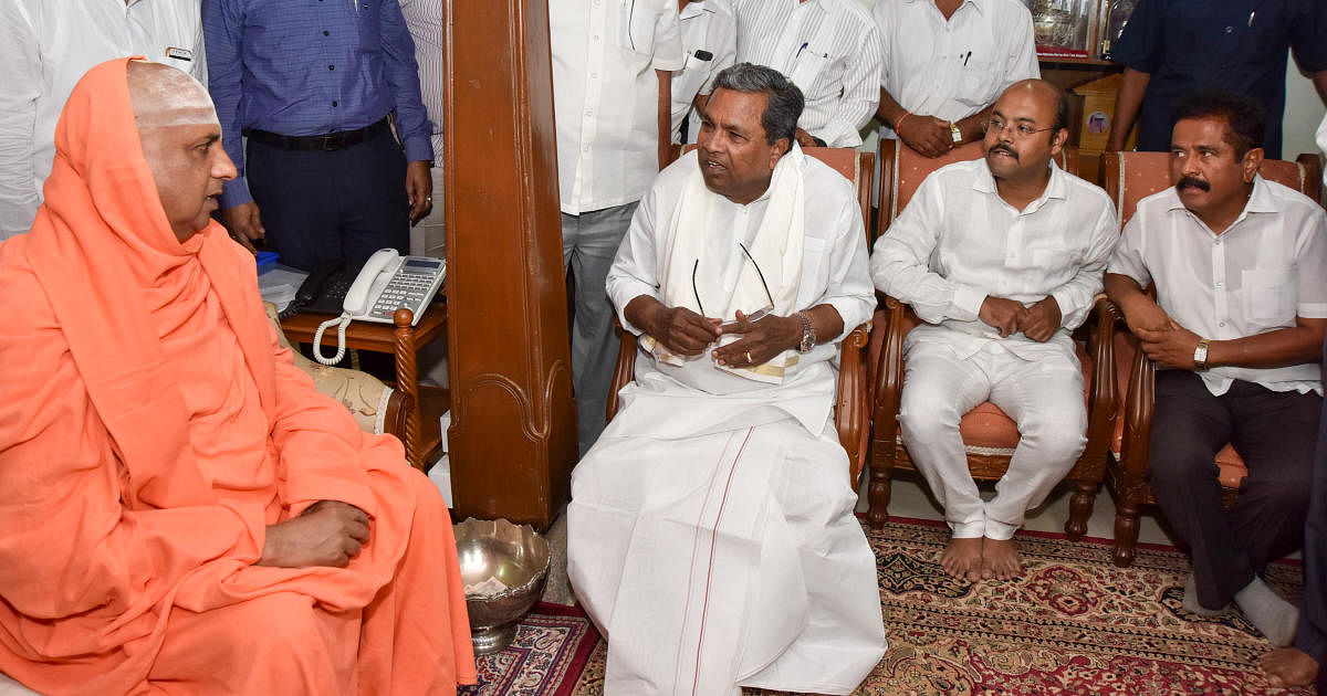 Suttur Mutt seer Shivarathri Deshikendra Swami has a word withseen with Chief Minister Siddaramaiah. Siddaramaiah's son Dr Yathindra, is seen at Suttur branch, in Mysuru on Friday. dh photo