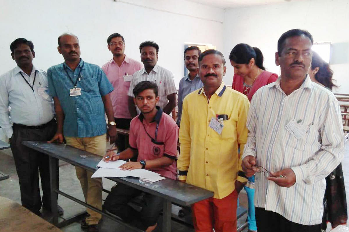 Student Prabhu Ram appears for Hindi language examination at Kottureshwara Pre-university College at Kottur in Ballari district on Friday. Some of the total 16 examination personnel are seen with him. DH photo