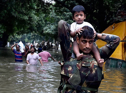 Army personnel carry children on their shoulders as they wade through flood waters in rain-hit Chennai on Thursday. PTI Photo