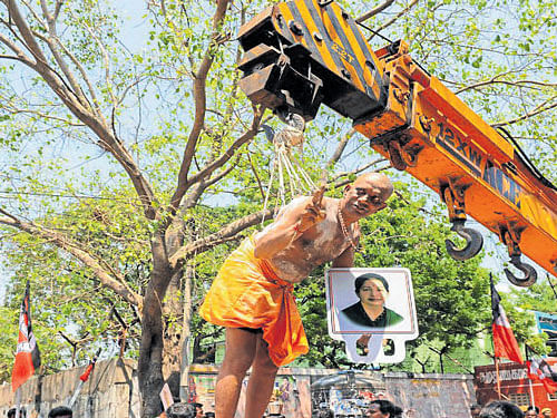 A man holds a portrait of Tamil Nadu Chief Minister  Jayalalithaa as he hangs from a crane held up with hooks pierced in the skin of his back, in a ritual meant for her  well-being as she remains hospitalised, in Chennai. AFP
